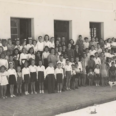 Boa parte dos moradores mais antigos do “bairro Lusitano” e da “Zona Tronca” estudou ali. Falamos do Grupo Escolar Municipal Clemente Pinto, fundado em 1º de agosto de 1939 pelo então prefeito Dante Marcucci.Sediado originalmente em uma casa de dois pavimentos de propriedade do sr. Pedro Tessari, na esquina das ruas Tronca e Marechal Floriano - onde funcionou uma das antigas sedes do Juventus e o lendário Bar Itália -, o colégio dispunha de quatro salas de aula na parte inferior, além de biblioteca e cozinha, no andar superior. Na foto: a Esquina das ruas Tronca e Marechal Floriano: alunos, professores e comunidade do Grupo Escolar Clemente Pinto, no início dos anos 1940. De gravata, na porta, o prefeito Dante Marcucci. <!-- NICAID(15729960) -->