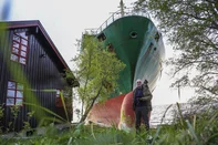 Johan Helberg poses next to his house and a 135-meter-long container ship by the shore in the Trondheimsfjord outside Byneset by Trondheim, Norway, on May 22, 2025, after the ship ran aground almost hitting his house. (Photo by Jan Langhaug / NTB / AFP) / Norway OUT<!-- NICAID(16044010) -->