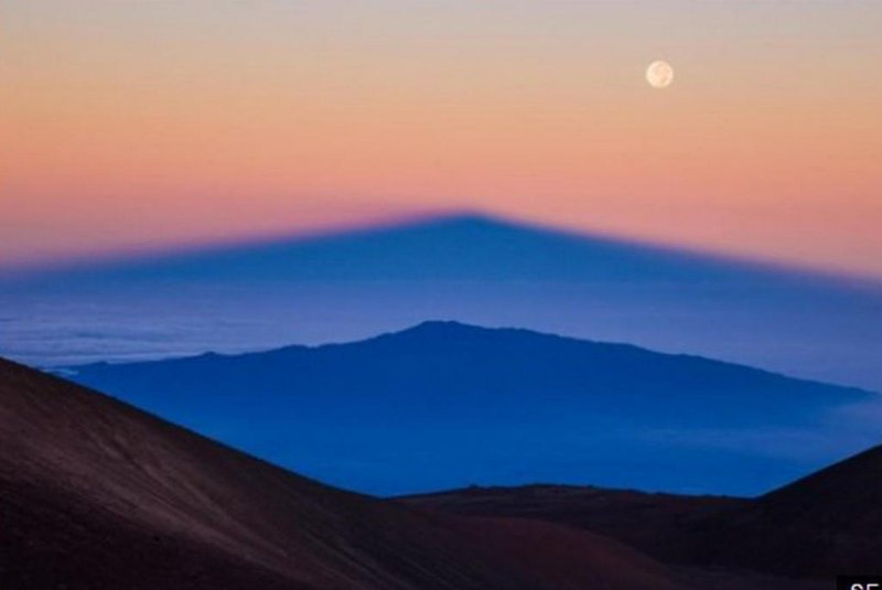  A sombra do vulcão Mauna Kea, no Havaí, é projetada pelo Sol nascente sobre outro vulcão, Hualalai, enquanto a Lua cheia brilha no céu, nesta imagem de Sean Goebel.