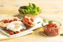 Salada de folhas com pão, homus, tomates assados e ovos pochê