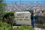 A tourist takes a picture of the citys panorama as he stands next to a wall with a graffito reading Tourist: your luxury trip - my daily misery at Park Guell on August 10, 2017 in Barcelona. Spanish activists in recent weeks have launched initiatives against what they consider a lack of control of mass tourism in cities like Barcelona and Palma de Mallorca, according to media reports. / AFP PHOTO / Josep LAGO