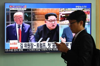 A man walks past a television news screen showing US President Donald Trump (L) and North Korean leader Kim Jong Un (C), at a train station in Seoul on June 11, 2018.Kim Jong Un and Donald Trump will meet on June 12 for an unprecedented summit in an attempt to address the last festering legacy of the Cold War, with the US President calling it a one time shot at peace. / AFP PHOTO / Jung Yeon-je