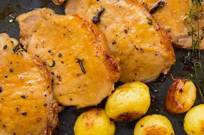 Na imagem,  quatro fatias de lombo cobertas com molho de mel e limão estão lado de pequenas batatas assadas