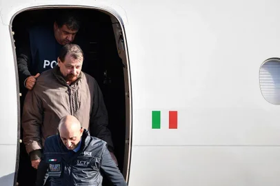  Italian former communist militant Cesare Battisti (C-L), wanted in Rome for four murders attributed to a far-left group in the 1970s, is escorted by Italian Police officers as he steps off a plane coming from Bolivia and chartered by Italian authorities, after landing at Ciampino airport in Rome on January 14, 2019. - Former communist militant Cesare Battisti landed in Rome on January 14 after an international police squad tracked the Italian down and arrested him in Bolivia, ending almost four decades on the run. (Photo by Alberto PIZZOLI / AFP)Editoria: POLLocal: RomeIndexador: ALBERTO PIZZOLISecao: politics (general)Fonte: AFPFotógrafo: STF