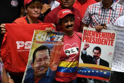 A supporter of Venezuelan President Nicolas Maduro displays placards with pictures of Maduro and late leader Hugo Chavez during a rally on May Day in Caracas on May 1, 2019. - Pro- and anti-government rallies were due to take place in Venezuela, a day after violent clashes erupted in the capital following opposition leader Juan Guidos call on the military to rise up against Maduro, who claimed the insurrection had failed. (Photo by Yuri CORTEZ / AFP)