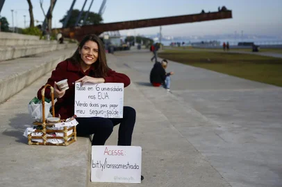  PORTO ALEGRE, RS, BRASIL, 02-07-2019: A estudante Larissa Migotto, 22 anos, com cesta de doces que vende na orla para pagar o seguro saúde para poder estudar nos Estados Unidos. Ela recebeu bolsa integral para estudar e trabalhar na Universidade de Illinois em Urbana-Champaign, mas precisa de 5 mil dólares para o seguro. Para juntar o dinheiro, a jovem iniciou vaquinha online e vende doces na capital. (Foto: Mateus Bruxel / Agência RBS)