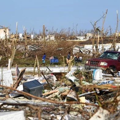 People push a shopping carts past debris in the Mudd neighbourhood in Marsh Harbor, Great Abaco, on September 7, 2019, in the aftermath of Hurricane Dorian. - Bahamians who lost everything in the devastating passage of Hurricane Dorian were scrambling Saturday to escape the worst-hit islands by sea or by air, after the historically powerful storm left at least 43 people dead with officials fearing a significantly higher toll. (Photo by Brendan Smialowski / AFP)