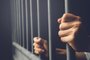  Man in prison hands of behind hold Steel cage jail bars. offender criminal locked in jail. filter dark vintage.Fonte: 255110735<!-- NICAID(14397646) -->