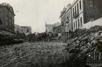 Rua Sinimbu, entre a Garibaldi e a Visconde de Pelotas, antes e depois das obras de rebaixamento, em 1940. Vê-se à esquerda, o prédio da antiga sede do Recreio da Juventude (posterior Farmácia do Círculo Operário Caxiense) e, na quadra seguinte, o prédio dos Correios, a antiga Casa Mandelli e, em frente, a Casa Bragagnolo. Ao fundo, à direita, a Casa Magnabosco e a Catedral Diocesana. À direita, em primeiro plano, a residência de João e Anna Mattana e, ao lado, a sede da Associação Rural de Caxias. Na esquina, o extinto prédio da loja Irmãos Calcagnotto, posteriormente Armarinhos Caxias e atualmente Casa & Cia. Mais acima também localizava-se a lendária Funerária Curtolo e, na esquina, a casa da família Serafini (em frente ao Magnabosco).<!-- NICAID(14463873) -->