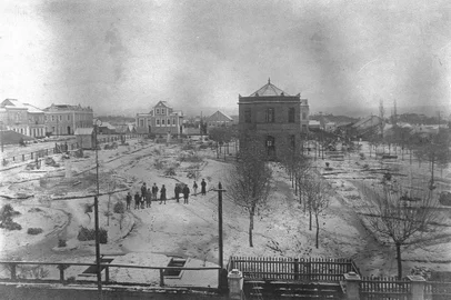 Neve cobrindo a Praça Dante Alighieri, com o ajardinamento realizado pelo Intendente Penna de Moraes. Ao centro o Chalet Municipal que abrigava um bar e restaurante. O município detinha a propriedade e a prestação de serviço era concessão de Jorge Arruda, o Buffete. Na parte inferior avista-se as entradas dos sanitários subterrâneos. Os sanitários apresentavam proposta moderna, construções subterrâneas com acessos individuais masculino e feminino. Data: 7 de junho de 1918. Ao fundo, a Rua Dr. Montaury.<!-- NICAID(14465473) -->