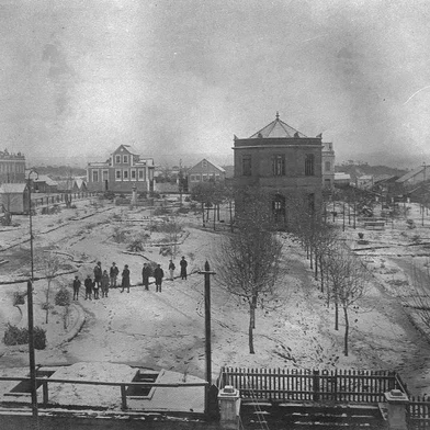Neve cobrindo a Praça Dante Alighieri, com o ajardinamento realizado pelo Intendente Penna de Moraes. Ao centro o Chalet Municipal que abrigava um bar e restaurante. O município detinha a propriedade e a prestação de serviço era concessão de Jorge Arruda, o Buffete. Na parte inferior avista-se as entradas dos sanitários subterrâneos. Os sanitários apresentavam proposta moderna, construções subterrâneas com acessos individuais masculino e feminino. Data: 7 de junho de 1918. Ao fundo, a Rua Dr. Montaury.<!-- NICAID(14465473) -->