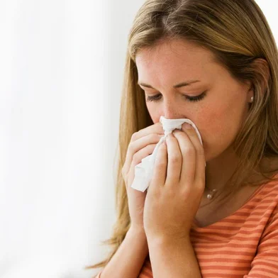 Beautiful young woman blowing her nose<!-- NICAID(10724836) -->