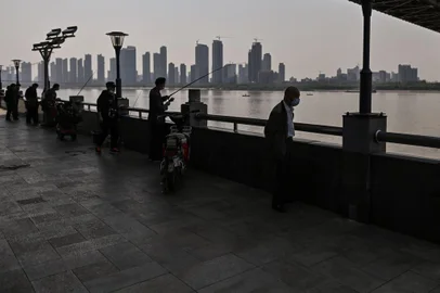 A man (C) wearing a face mask fishes next to Wuhan Bridge in Yangtze River in Wuhan, on April 9, 2020. (Photo by Hector RETAMAL / AFP)<!-- NICAID(14473221) -->