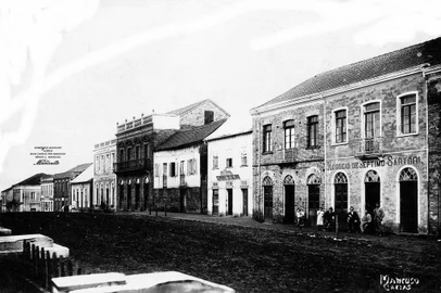 Na foto, registrada por Domingos Mancuso em meados de 1908, vemos alguns dos prédios citados por João Spadari Adami em seu texto de 1962. Trata-se do trecho da Avenida Júlio de Castilhos (a antiga Silveira Martins) em frente à Praça Dante, com os negócios da família Sartori (posterior Cine Central, em primeiro plano) e a residência e Fábrica de Salame e Presunto de Angelo Chittolina (atual Super Andreazza). Entre os dois, os casarões que cederam espaço ao Condomínio Galeria Auto João Muratore (o famoso Caixa de Fósforo) e à Galeria do Comércio, ligando a Júlio à Pinheiro Machado.<!-- NICAID(14531869) -->