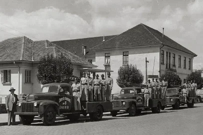 O comandante Frederico Bergmann (à esquerda) com os bombeiros e os clássicos modelos Ford na Rua Sinimbu, próximo à Coronel Flores, onde ficava a antiga sede. O prédio à direita abrigava, no piso superior, a Congregação das Irmãs Carlistas (Colégio São Carlos). No térreo, o alojamento da Brigada Militar e dos bombeiros.  A partir da esquerda vê-se o então comandante Frederico Bergmann, o sargento Oscar de Azevedo, Nei Andrade, Artur Mello, Joecy da Silva, Candido Abreu e João Maria Machado, entre outros não identificados. Os veículos Ford 1946/1948 eram modelos auto-bomba-tanque.<!-- NICAID(14537762) -->