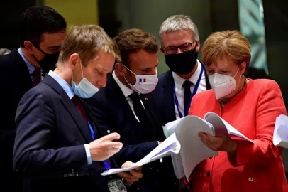 Spains Prime Minister Pedro Sanchez (L), French President Emmanuel Macron (C) and German Chancellor Angela Merkel (R) look into documents during an EU summit in Brussels on July 20, 2020, as the leaders of the European Union hold their first face-to-face summit over a post-virus economic rescue plan. (Photo by JOHN THYS / POOL / AFP)