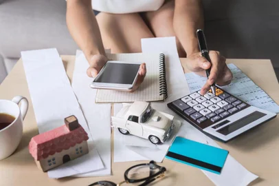 Young woman using smart phone and checking bills, taxes, bank account balance and calculating expenses in the living room at homecontabilidade, escritorio, calculos, calculadora, finanças. Foto: Kittiphan /  stock.adobe.comFonte: 220613223<!-- NICAID(14555710) -->