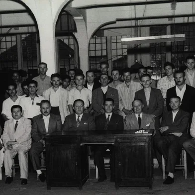 Graciano Fillippini ladeado pelos diretores Júlio João Eberle (E) e Caetano Pettinelli, durante o seu jubileu de prata na empresa, em 21 de janeiro de 1957. À primeira fila estão, entre outros, Humberto Bassanesi e Alcides Fedrizzi.<!-- NICAID(14575992) -->