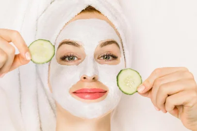 Home spa, skin care concept. Close up top portrait of pretty young woman with towel on her head, white clay mask on her face, holding pieces of fresh cucumber, lying on the isolated white background.Tratamentos de beleza caseiros com pepinos, máscara, pele, rosto. Foto:sofiko14  / stock.adobe.comFonte: 337738430<!-- NICAID(14591017) -->