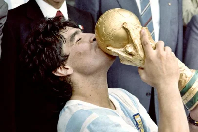 (FILES) In this file picture taken on June 29, 1986 Argentina's football star team captain Diego Maradona kisses the World Soccer Cup won by his team after a 3-2 victory over West Germany at the Azteca stadium in Mexico City watched by Mexican President Miguel de La Madrid (L) and West German Chancellor Helmut Kohl. - Argentine football legend Diego Maradona turns 60 on October 30, 2020. (Photo by STAFF / AFP)<!-- NICAID(14629180) -->
