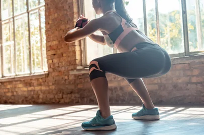 Young fit woman doing squats fitness exercise in gym, rear closeup viewYoung fit sporty active athlete woman wear sportswear crouching doing squats session fitness training legs buttocks muscles workout exercise in modern sunny gym space indoors, rear back close up viewFonte: 317176436<!-- NICAID(14646771) -->