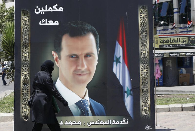 A woman walks past an election campaign billboard depicting Syrian President Bashar al-Assad, a candidate for the upcoming presidential vote, in the capital Damascus, on May 24, 2021. - The Syrian President Bashar al-Assad, whose family has ruled the country for over half a century, faces an election on May 26 meant to cement his image as the only hope for recovery in the war-battered country, analysts say. In the ballot, two challengers will run against him, approved by an Assad-appointed constitutional court, out of a total of 51 applicants. (Photo by LOUAI BESHARA / AFP)<!-- NICAID(14792453) -->