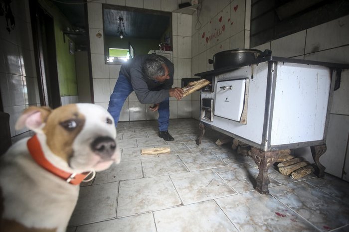 Sob o olhar atento do cachorro Thor, Alfredo Nogueira abastece o fogão com lenha para cozinhar mondongo