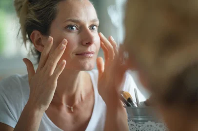 Portrait of woman looking at her face in mirrorFonte: 294362865<!-- NICAID(14910103) -->
