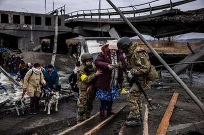 Ukrainian soldiers help an elderly woman to cross a destroyed bridge as she evacuates the city of Irpin, northwest of Kyiv, on March 7, 2022. - Ukraine dismissed Moscows offer to set up humanitarian corridors from several bombarded cities on Monday after it emerged some routes would lead refugees into Russia or Belarus. The Russian proposal of safe passage from Kharkiv, Kyiv, Mariupol and Sumy had come after terrified Ukrainian civilians came under fire in previous ceasefire attempts. (Photo by Dimitar DILKOFF / AFP)Editoria: WARLocal: IrpinIndexador: DIMITAR DILKOFFSecao: refugeeFonte: AFPFotógrafo: STF<!-- NICAID(15034868) -->